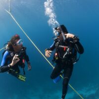 Two divers underwater. One signals to the other they are experiencing ear problems.