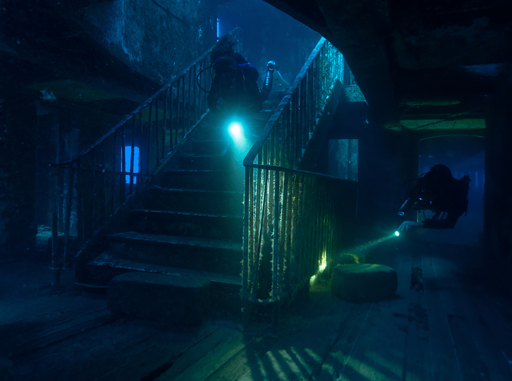 Two scuba divers swimming through the iconic staircase of the Karwela wreck in Malta, one of the best destinations for August