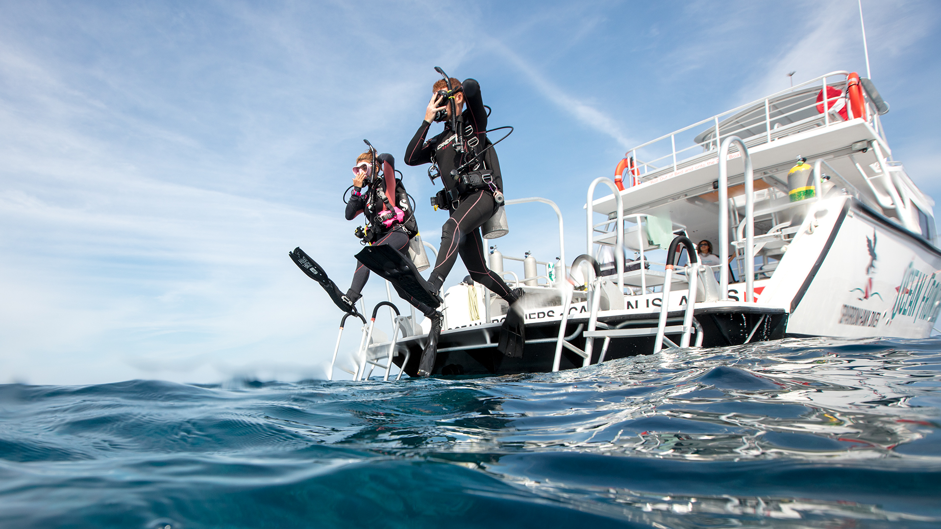 Two scuba divers entering the water; in the English language you can either say they dived into or dove into the water