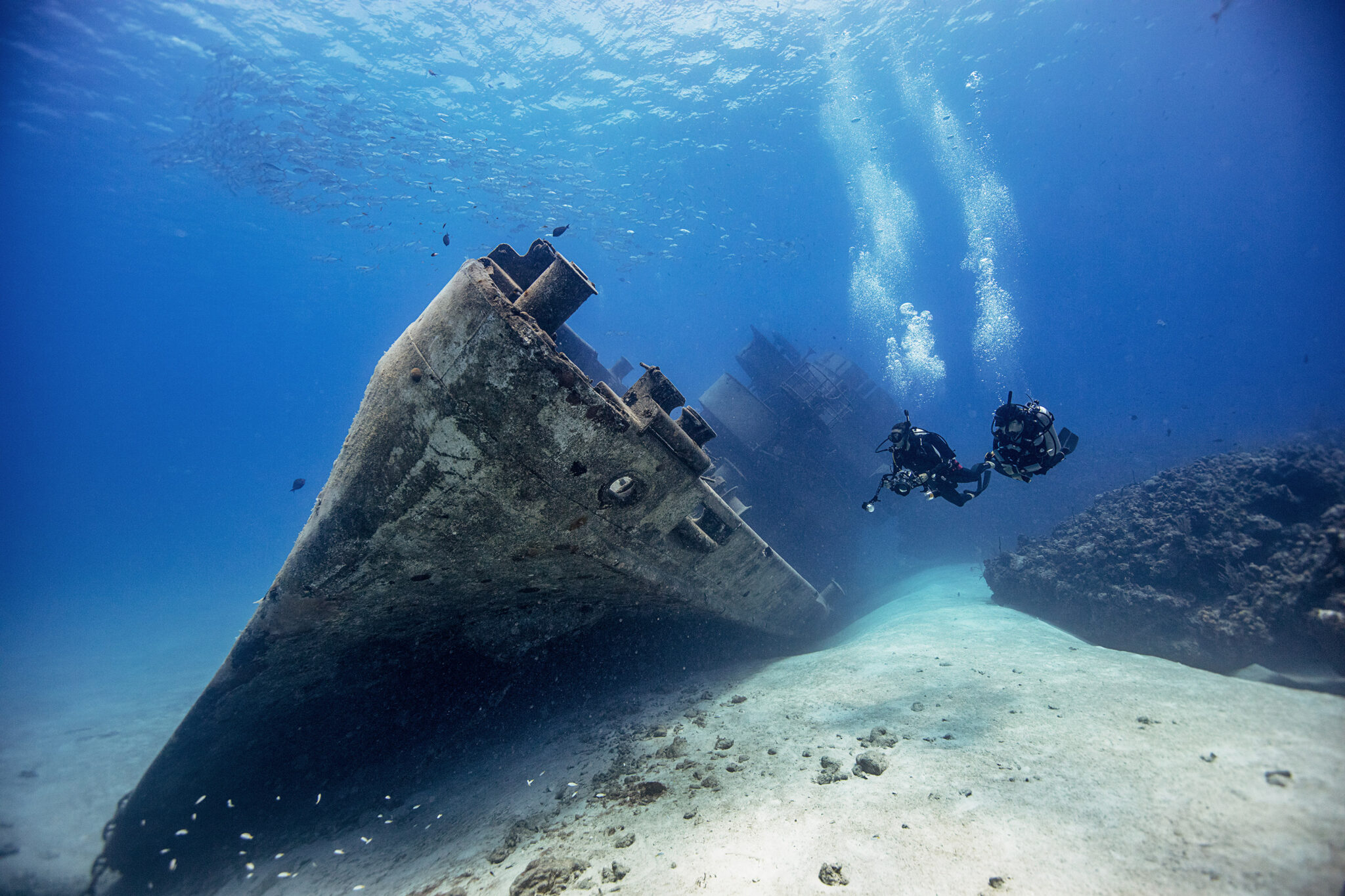 Two scuba divers swimming by the USS Kittiwake shipwreck in the Cayman Islands, a hotspot for incredible scuba vacations