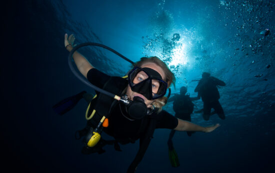 a scuba diver looking down at the camera while other divers hover above