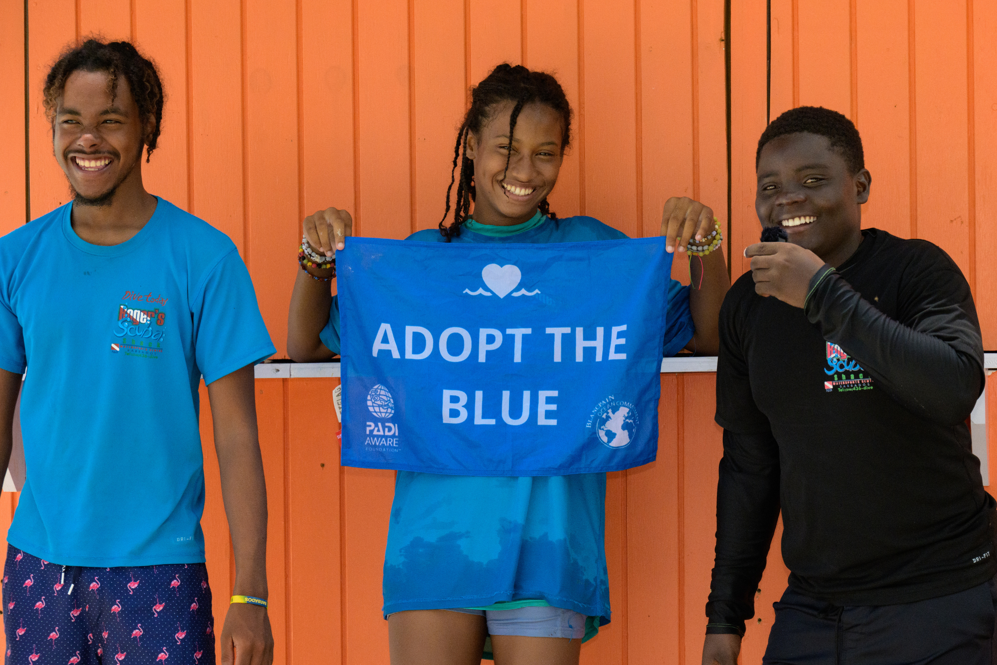 Drei Personen halten die Adopt the Blue-Flagge und unterstützen den Schutz der Meere