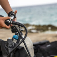 A diver attaches the first stage of their regulator to a tank