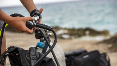 A diver attaches the first stage of their regulator to a tank