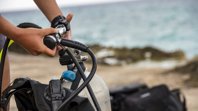 A diver attaches the first stage of their regulator to a tank