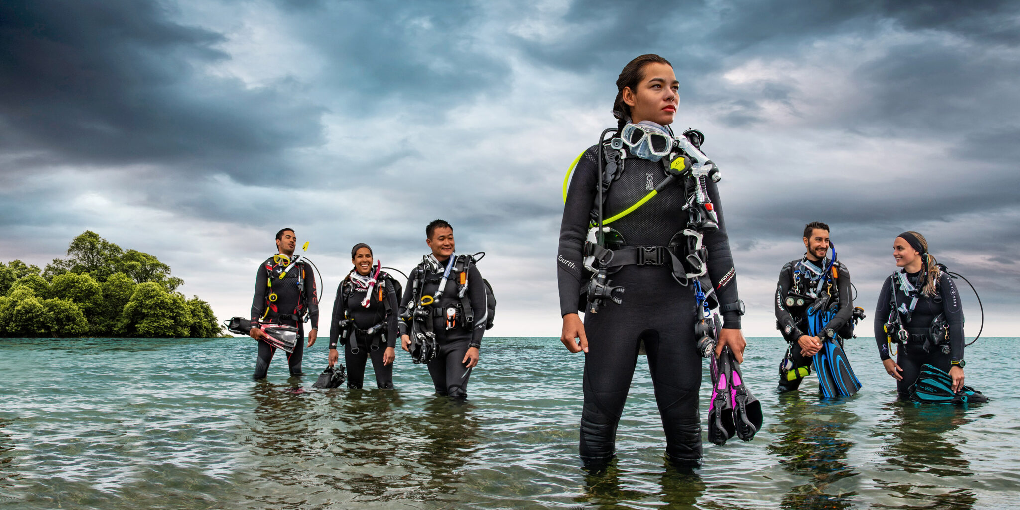 A Professional diver standing in shallow water with three scuba students behind as they exit from a shore dive at the beach