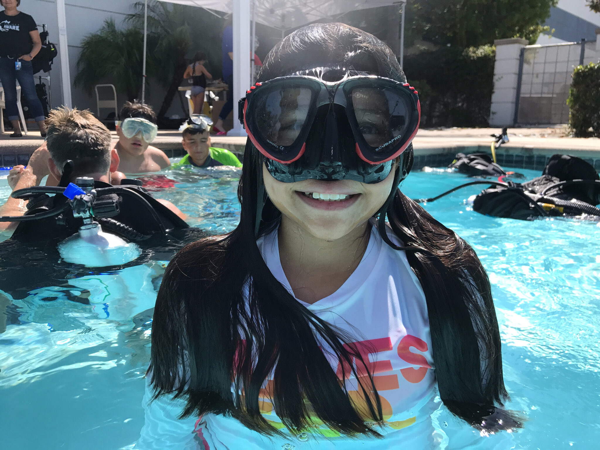 a smiling girl wearing a scuba mask standing in an outdoor pool