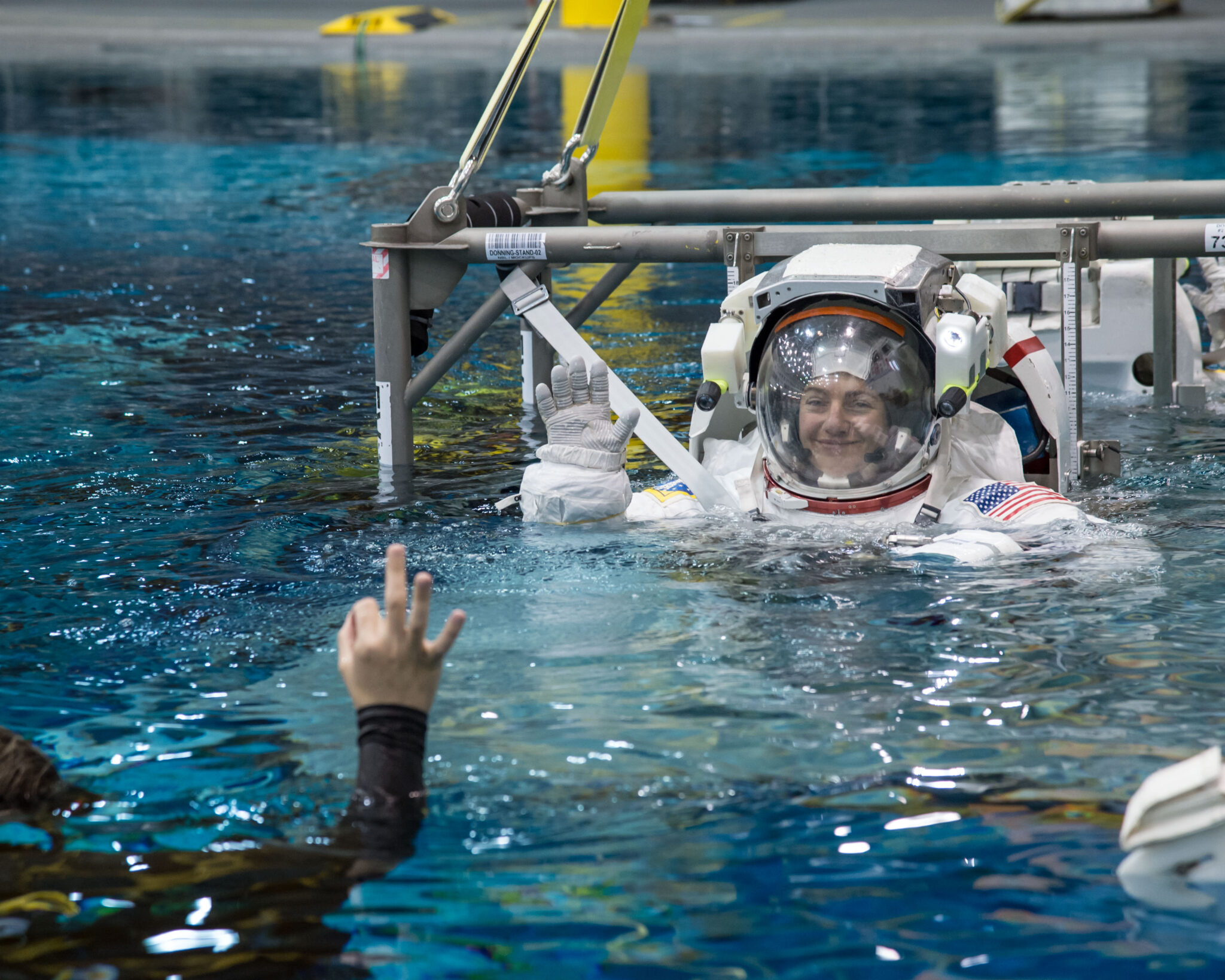 A female astronaut in a EVA suit smiles and waves to a scuba diver