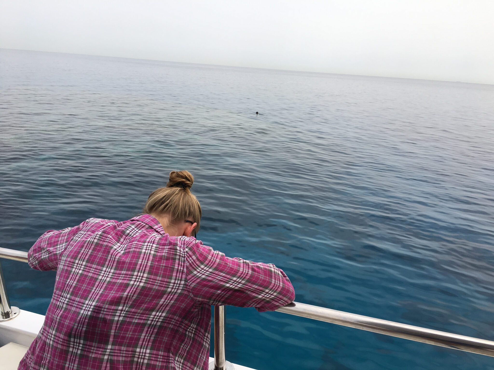 A scuba diver in a pink shirt suffering from seasickness is leaning over the side of the boat and throwing up after diving