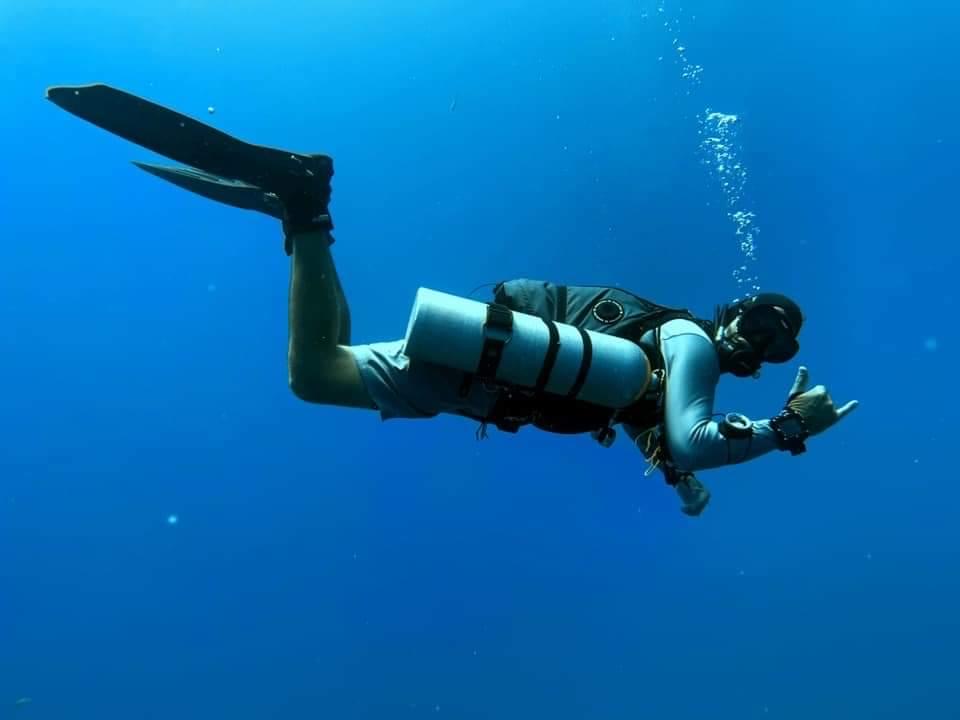 A diver floats in the blue diving with twin tanks in the sidemount style