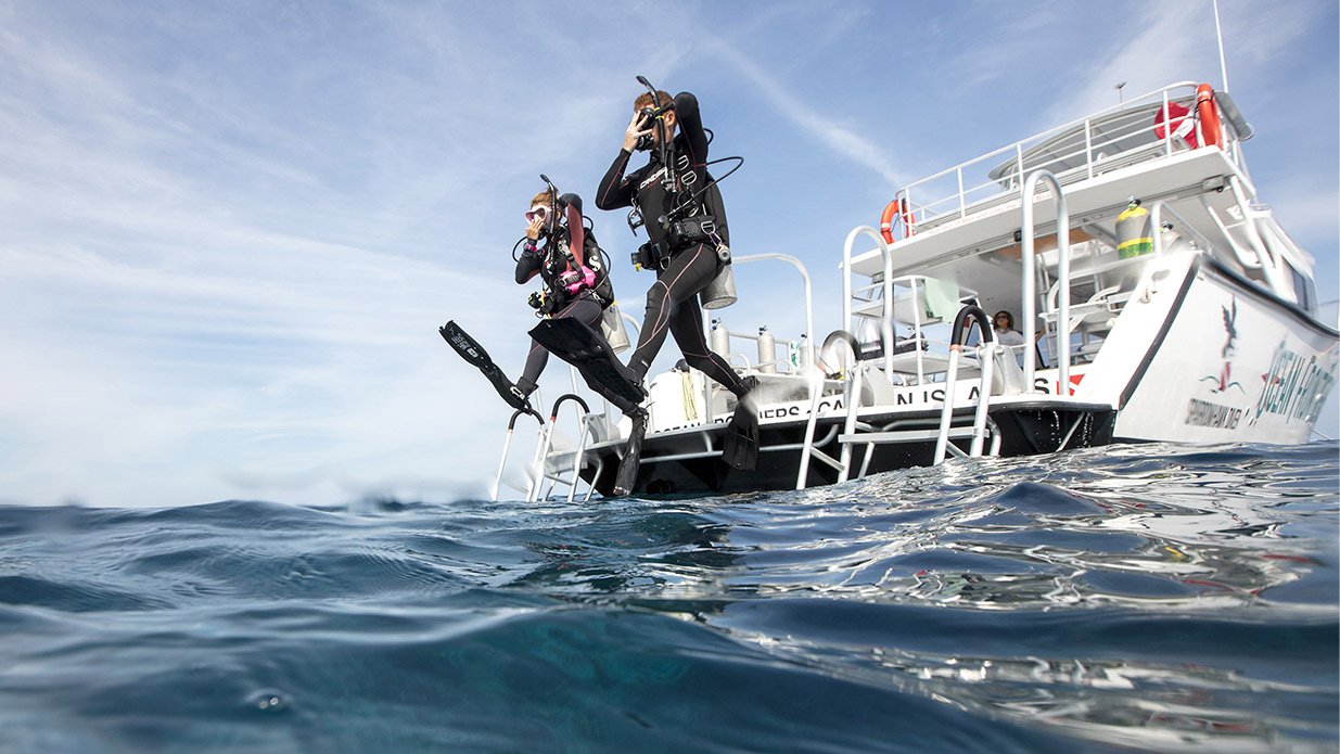 Two scuba divers jumping into the ocean from a dive boat using a stride entry as part of a PADI ReActivate scuba refresher