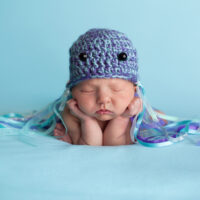 A sleeping newborn baby wearing a crocheted hat decorated as a jellyfish costume and one of the best ocean costumes for kids