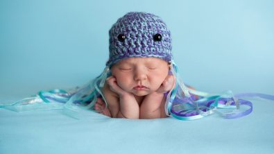 A sleeping newborn baby wearing a crocheted hat decorated as a jellyfish costume and one of the best ocean costumes for kids