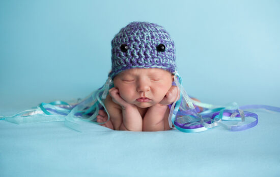 A sleeping newborn baby wearing a crocheted hat decorated as a jellyfish costume and one of the best ocean costumes for kids