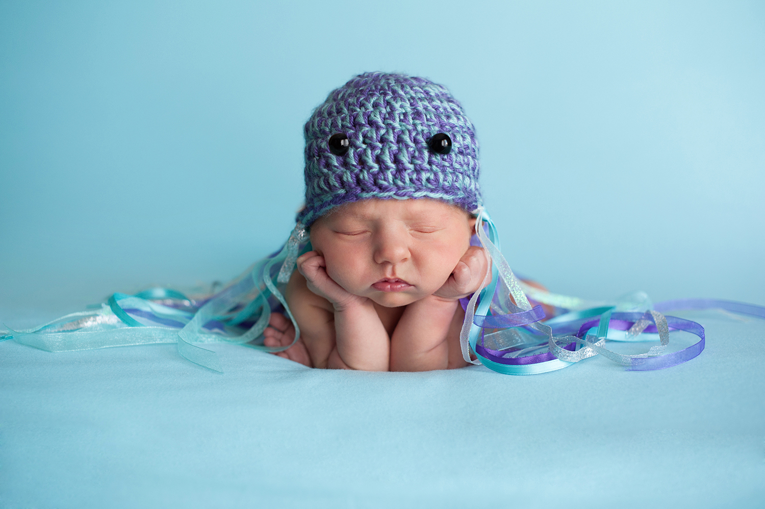 A sleeping newborn baby wearing a crocheted hat decorated as a jellyfish costume and one of the best ocean costumes for kids