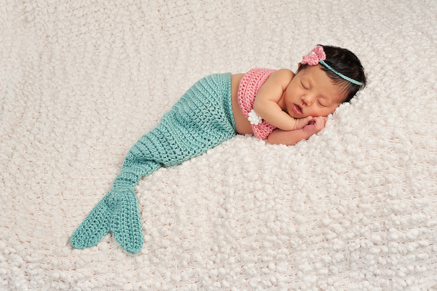 A sleeping newborn baby wearing a green crocheted mermaid tail which is one of the best ocean costumes for kids
