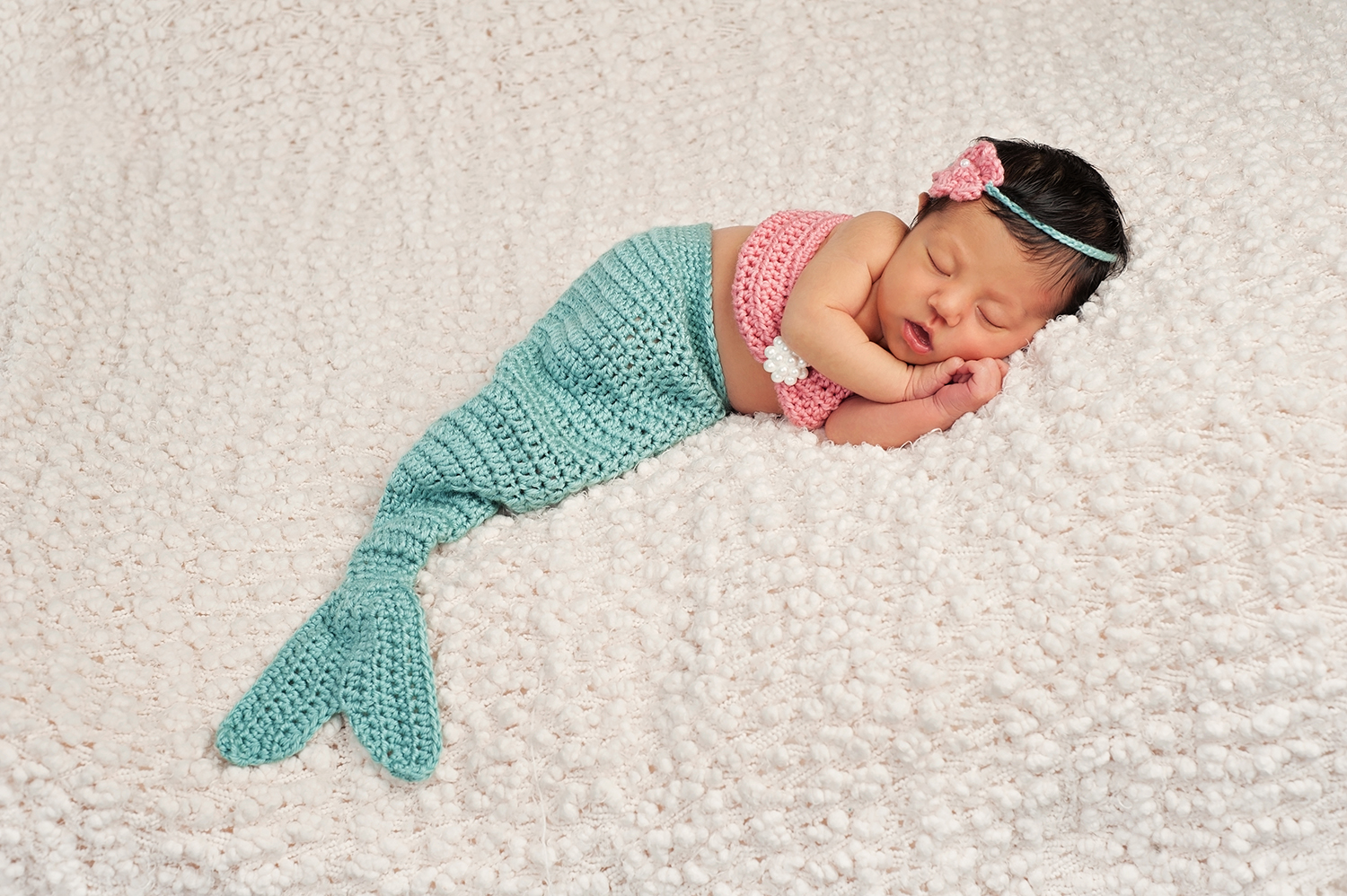 A sleeping baby in a crocheted mermaid tail, whose parents probably want to know answers to 'what are cute ocean names?'