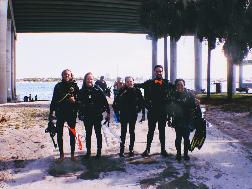Divers stand with their gear in front of the Blue Heron Bridge in Florida.