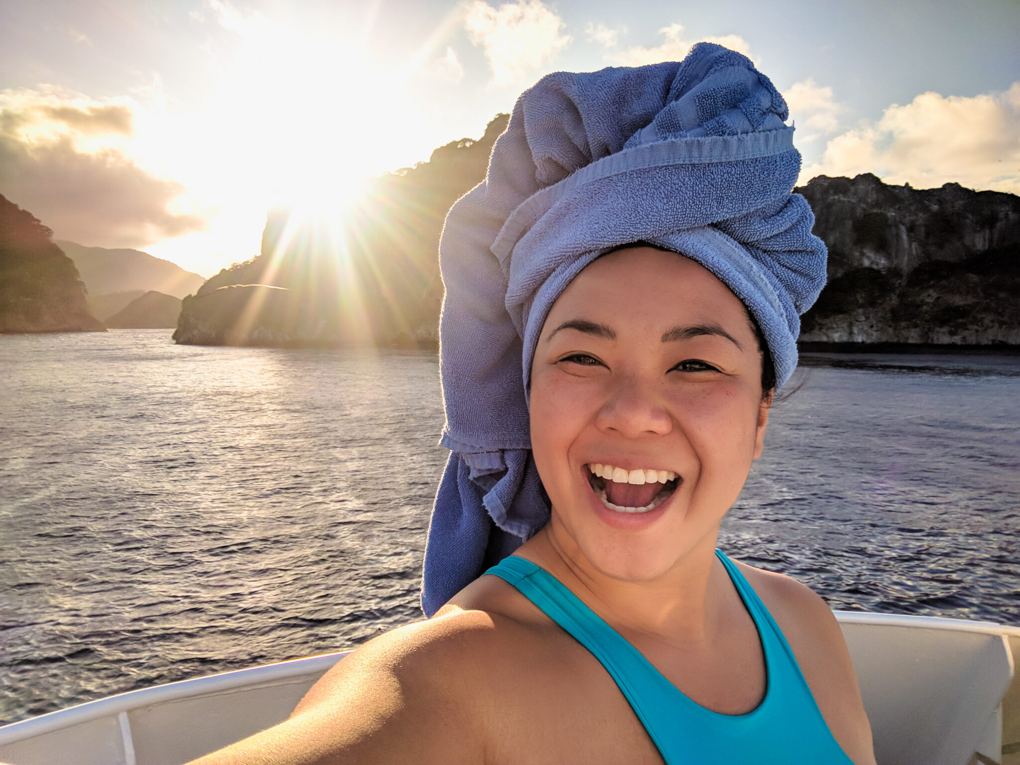 A woman smiles with a towel wrapped on her head with a sunset in the background