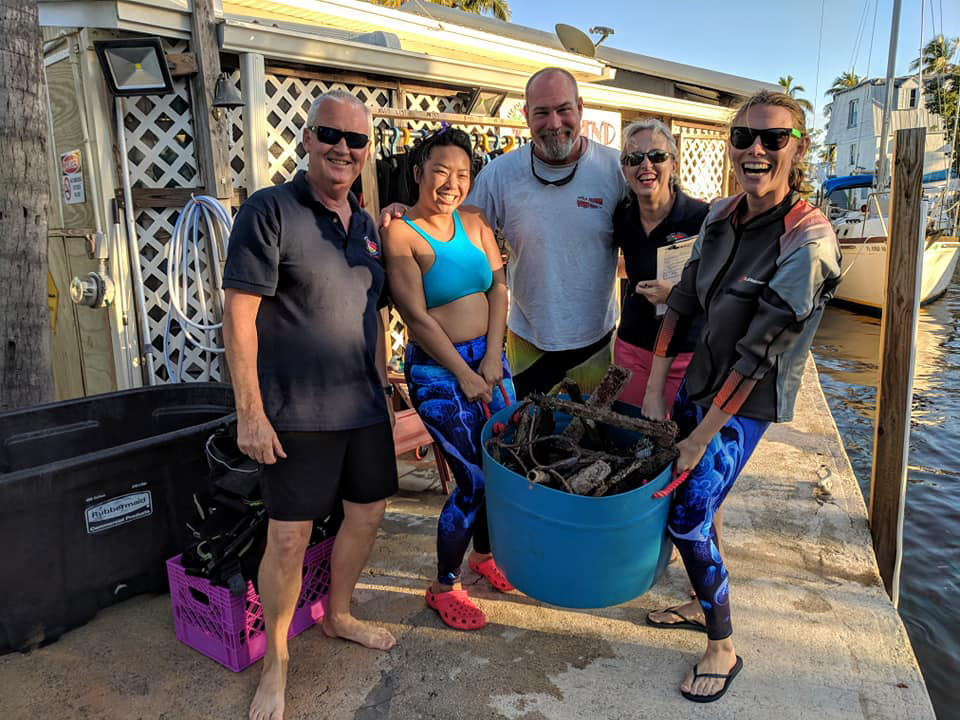 People smiling while holding a bucket full of rope taken off the seafloor