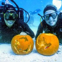 Two divers smile with pumpkins underwater