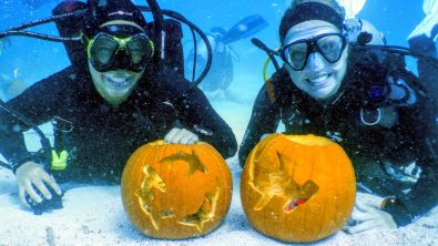 Two divers smile with pumpkins underwater