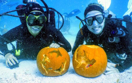Two divers smile with pumpkins underwater