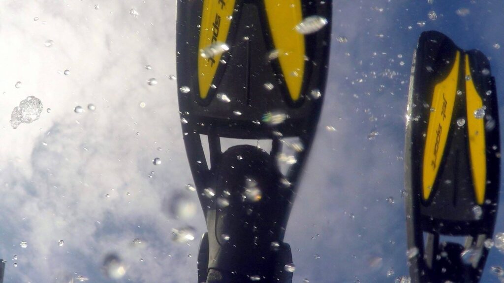 A diver's fin tips are seen against the sky as she tips over a boat edge.