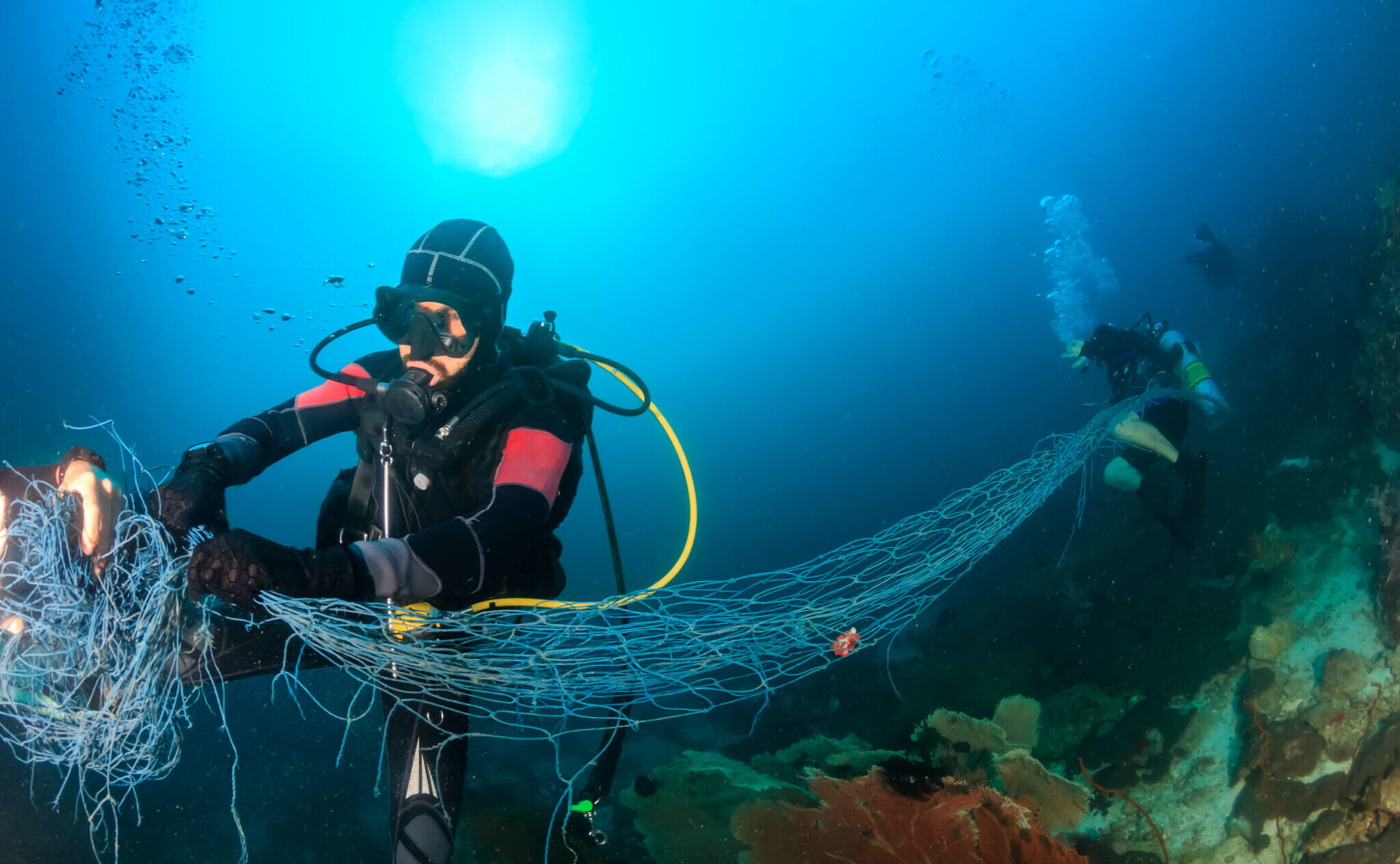 Scuba divers removing a big ghost fishing net from the reef, one of many amazing marine stories when it comes to conservation