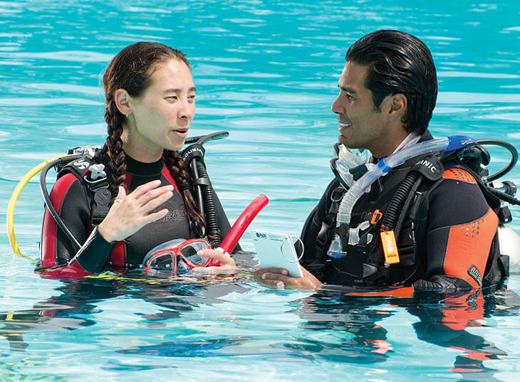 a diver talks to her scuba instructor while standing in a pool