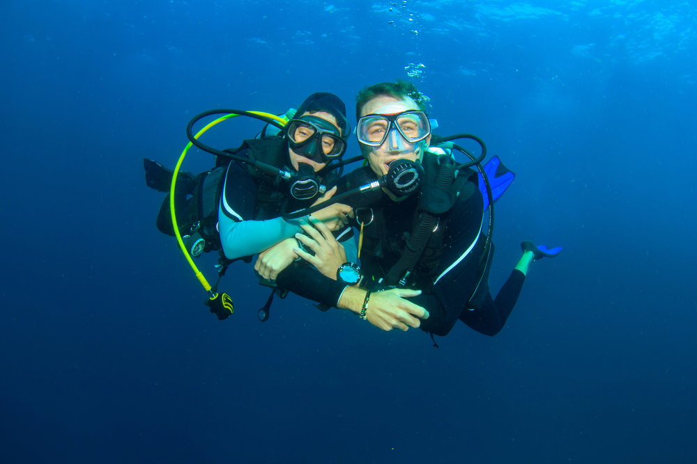 A scuba diver holding onto their buddy, which helps maintain your position underwater when sneezing or vomiting while diving