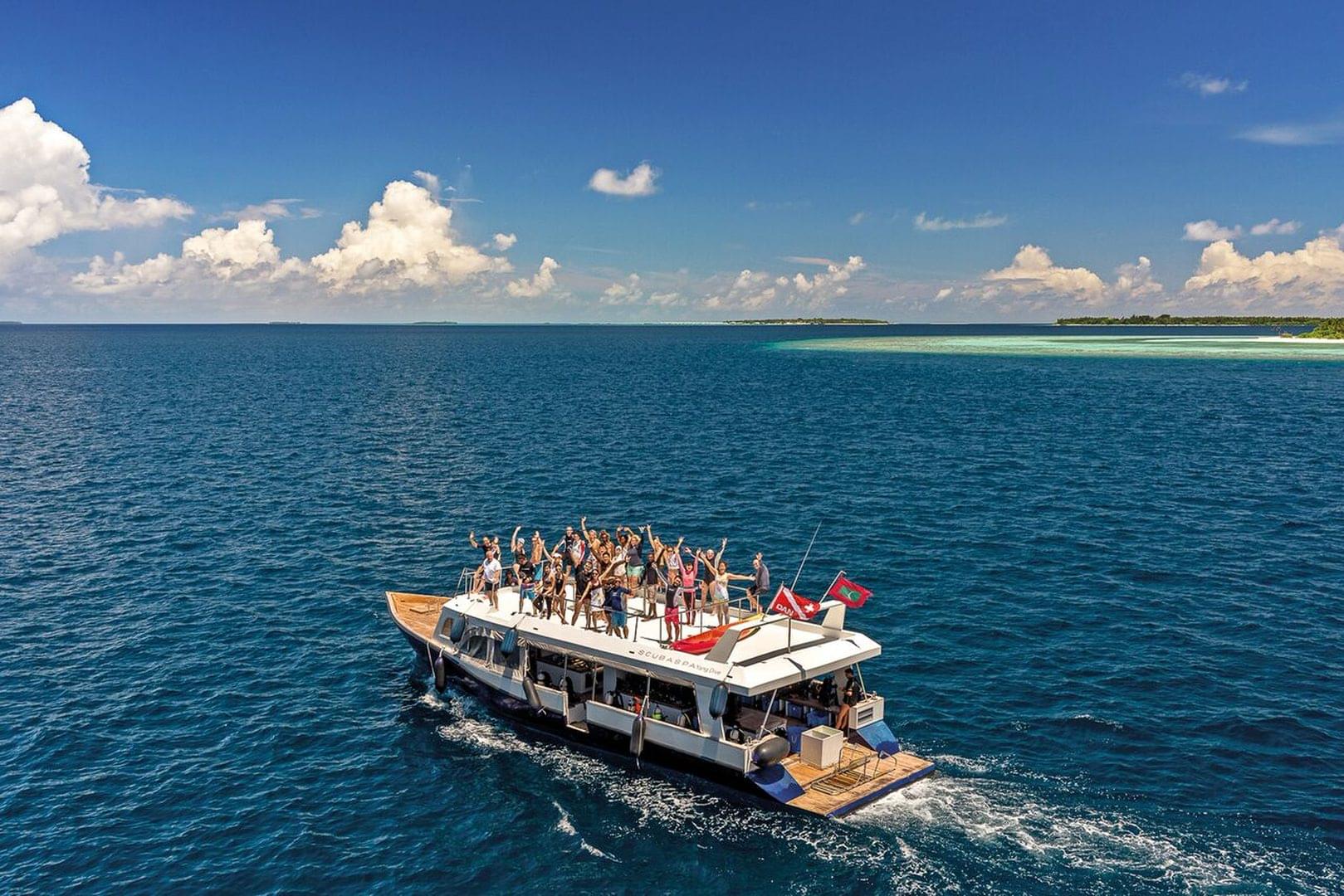 A group of happy scuba divers celebrating together on top of a dhoni boat while on vacation in the Maldives