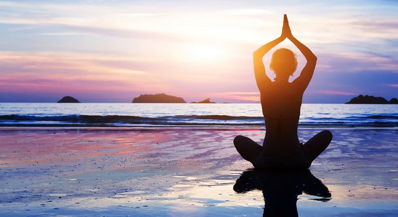 A woman does a yoga pose as the sun sets over the water