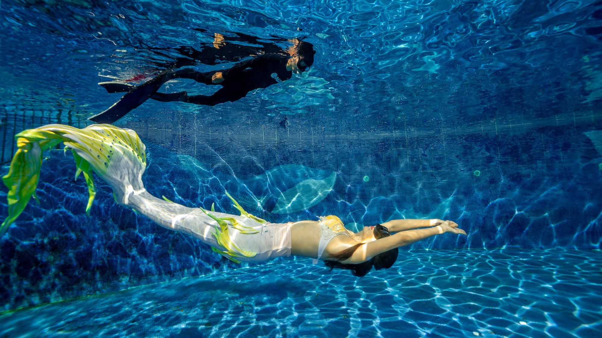 Padi mermaid instructor swimming underwater with a safety diver on the surface