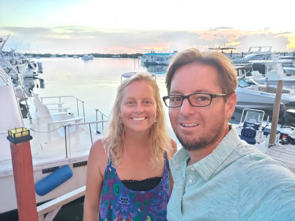 Two divers smile near a dock at sunset