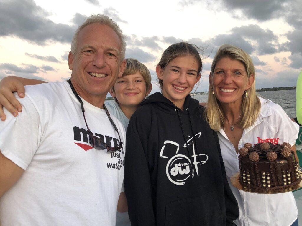 A family huddles together, smiling with the ocean in the background