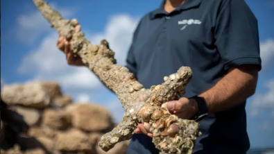 A man holds a crusader's sword encrusted with marine life