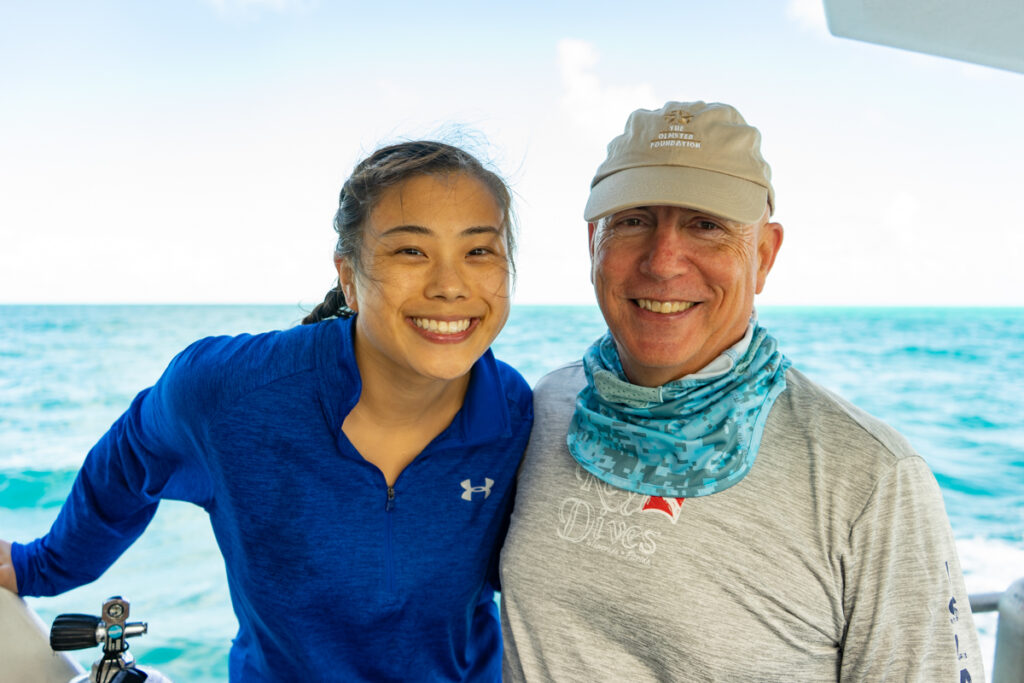 Jackie and Kurt Tidd smile on a dive boat with the ocean in the background