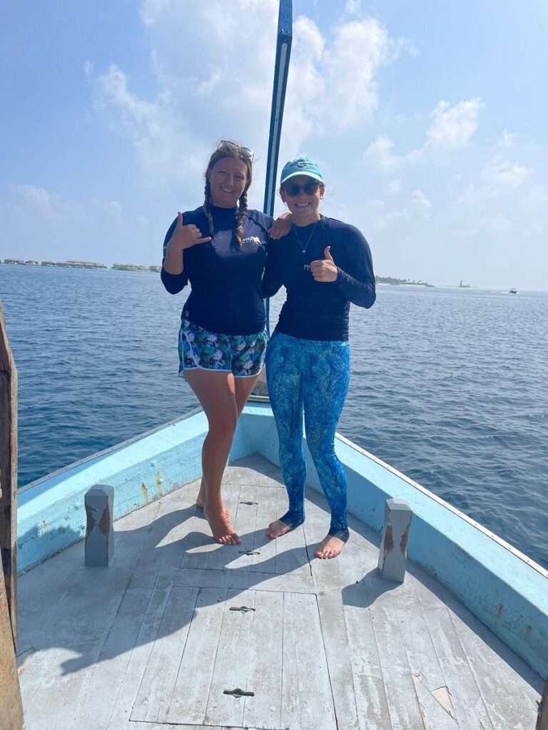 Two scientists give positive hand signals standing on the bow of a research boat.