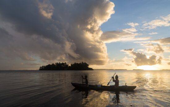 two people in a canoe at sunset in the solomon islands