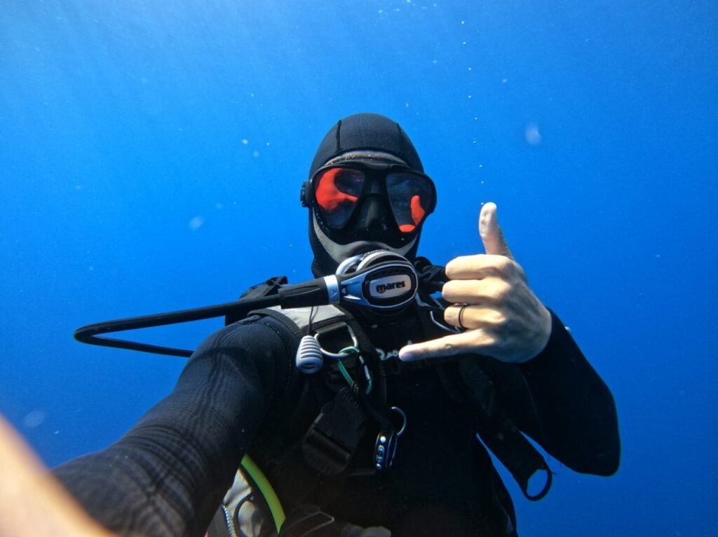 A diver holds up the hand signal for a rad dive while underwater.