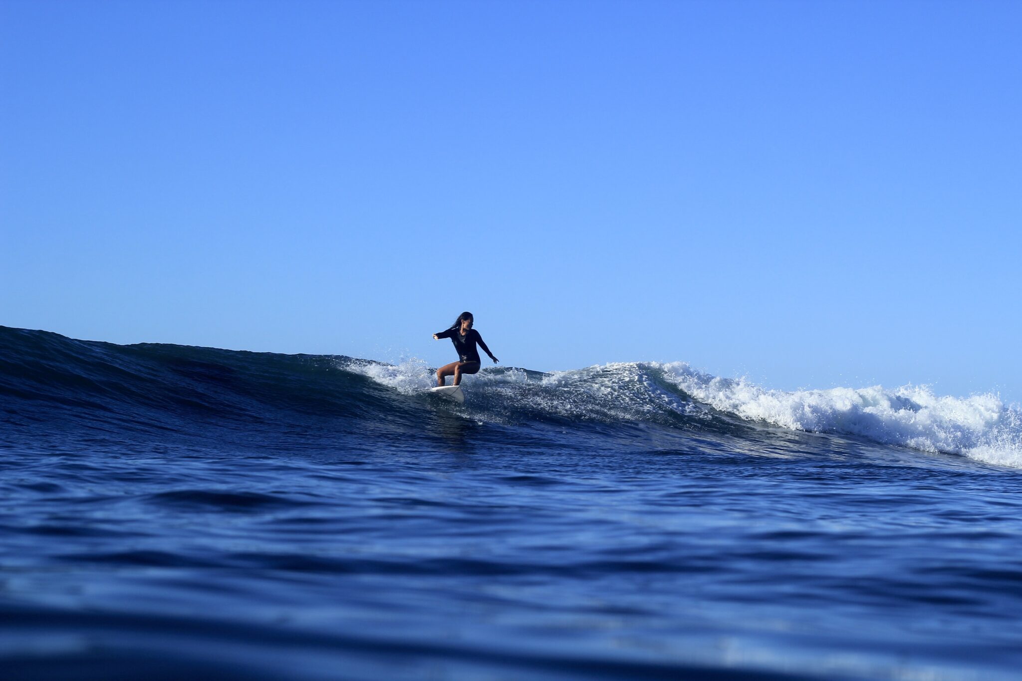 A woman rides the crest of a wave in El Salvador on her surfboard.