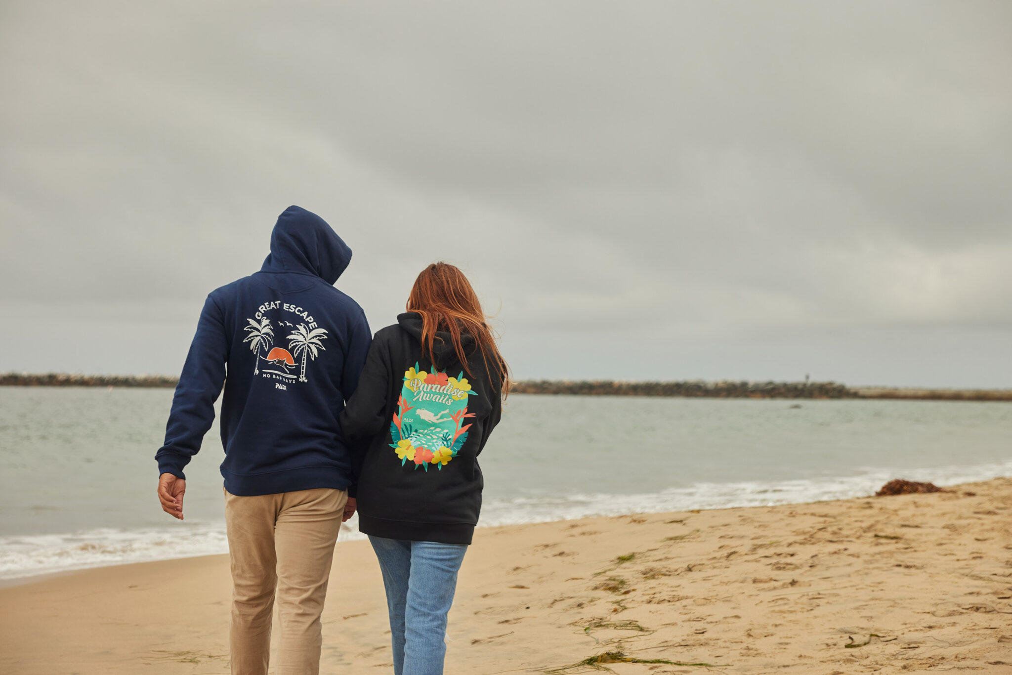 two people walk on the beach wearing PADI Gear