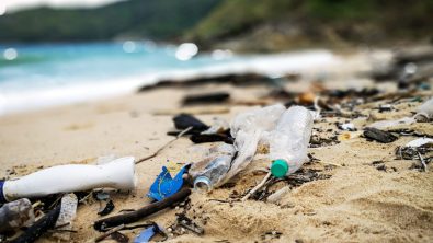 Plastic pollution and other trash scattered on a beach, with ocean in the background