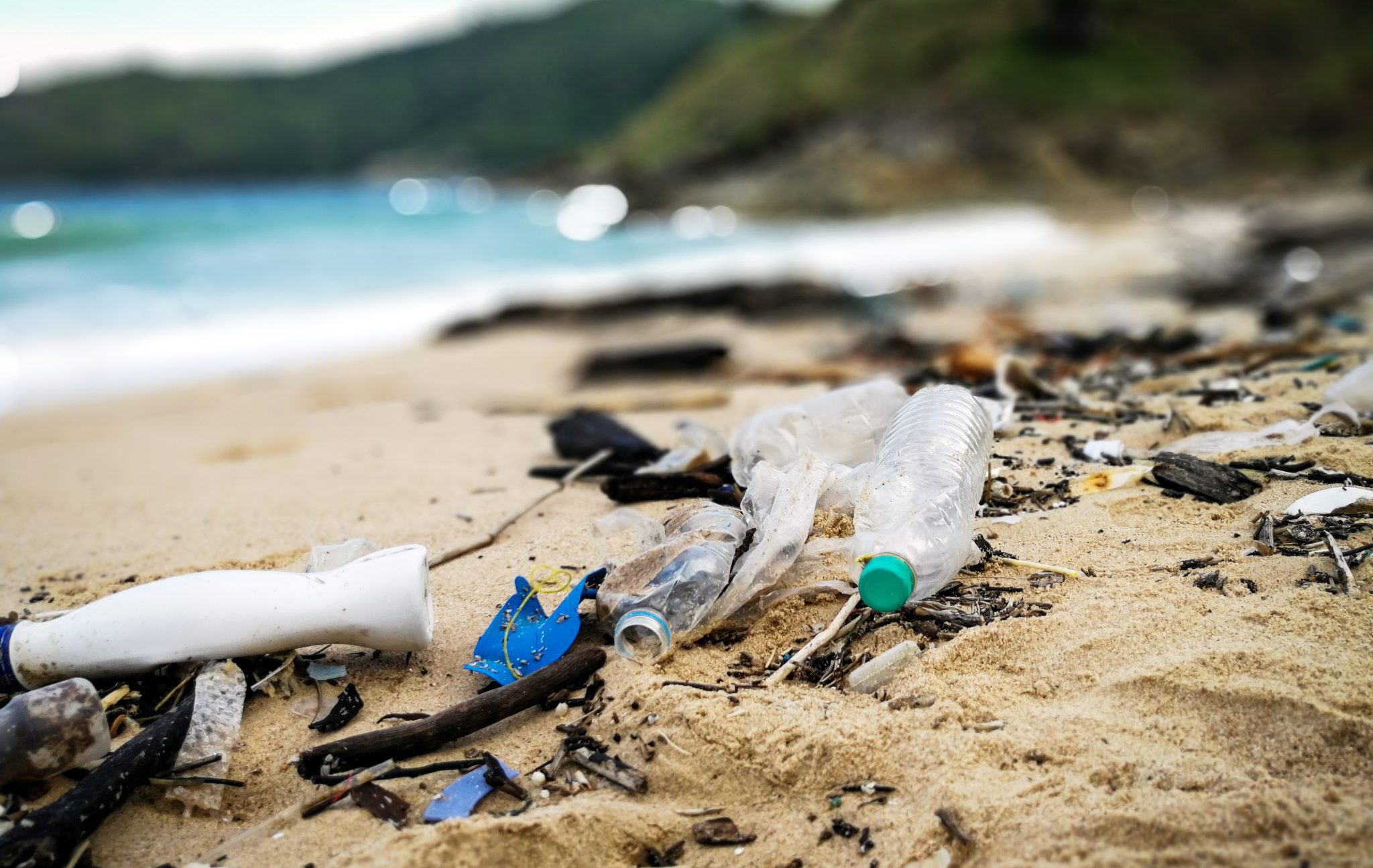 Plastic pollution and other trash scattered on a beach, with ocean in the background