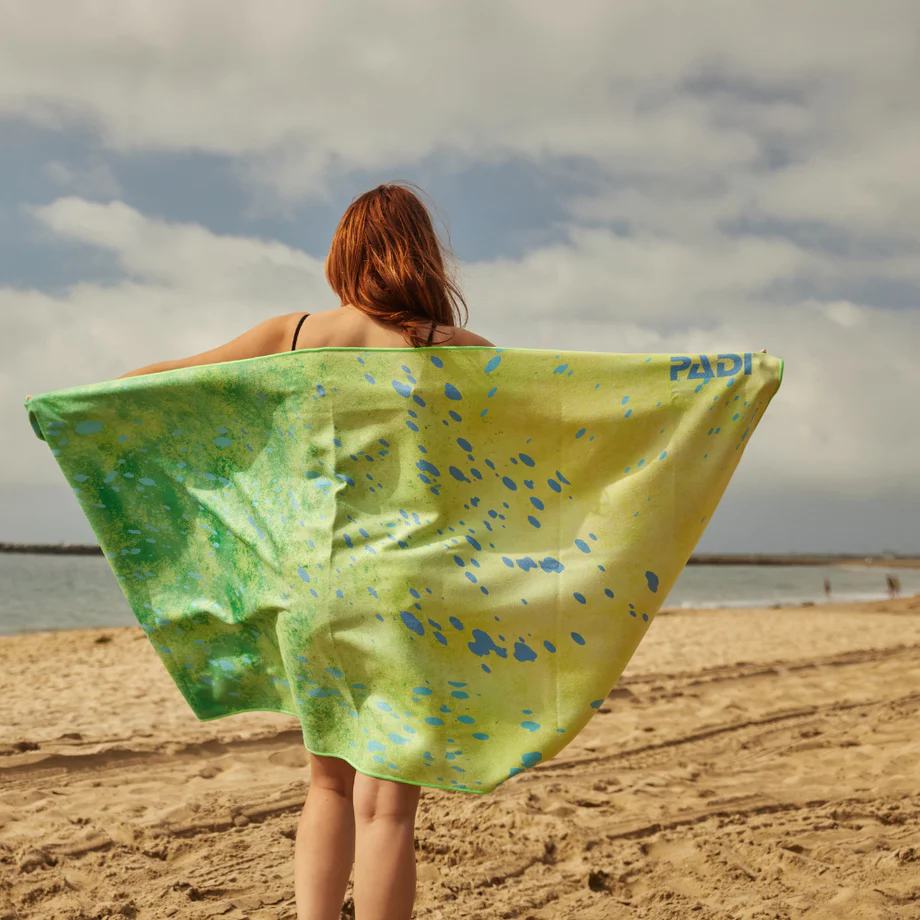 a woman holds a dorado print towel on the beach
