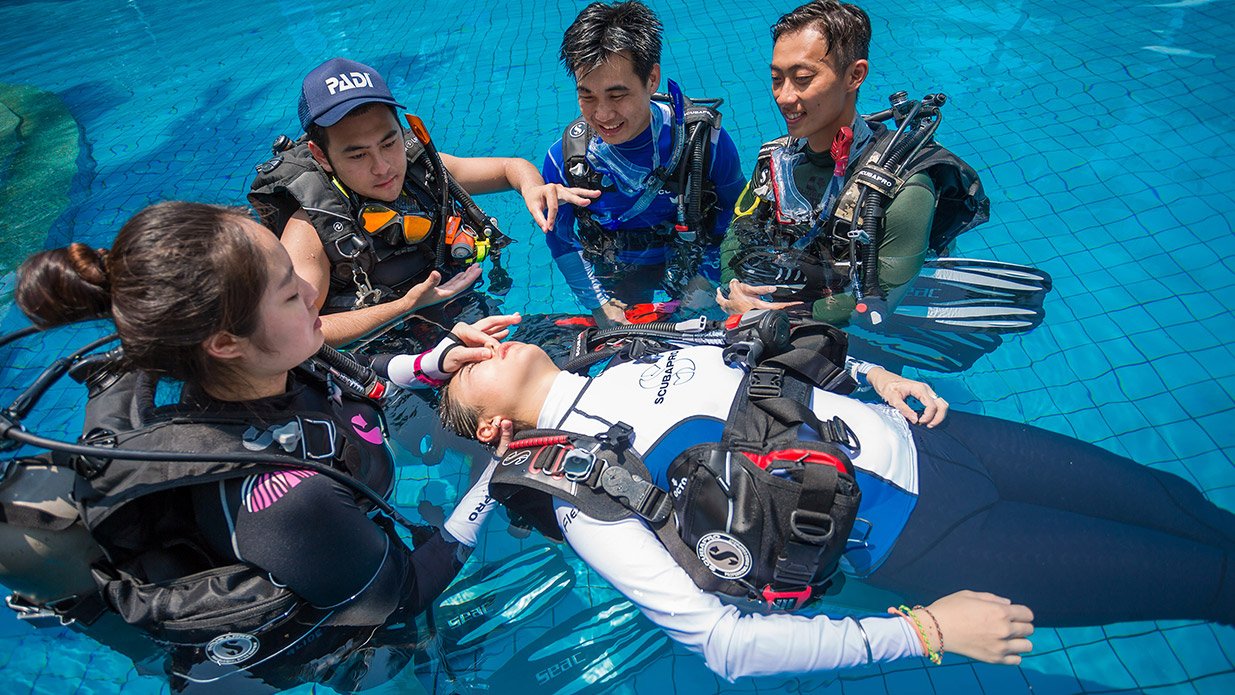 A PADI Instructor teaches a group of scuba diving students how to do rescue breaths during their PADI Rescue Diver course