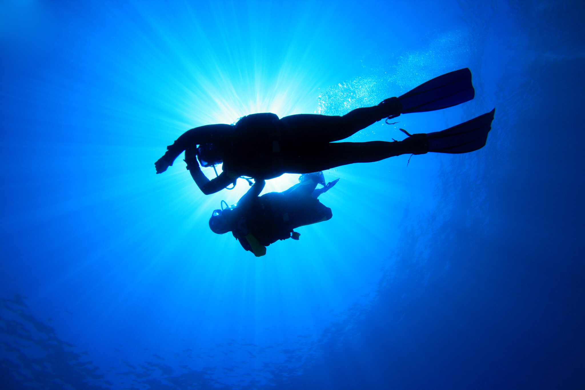 A silhouette of a scuba student under the surface of the ocean with a PADI Instructor, one of the top dive jobs in the world