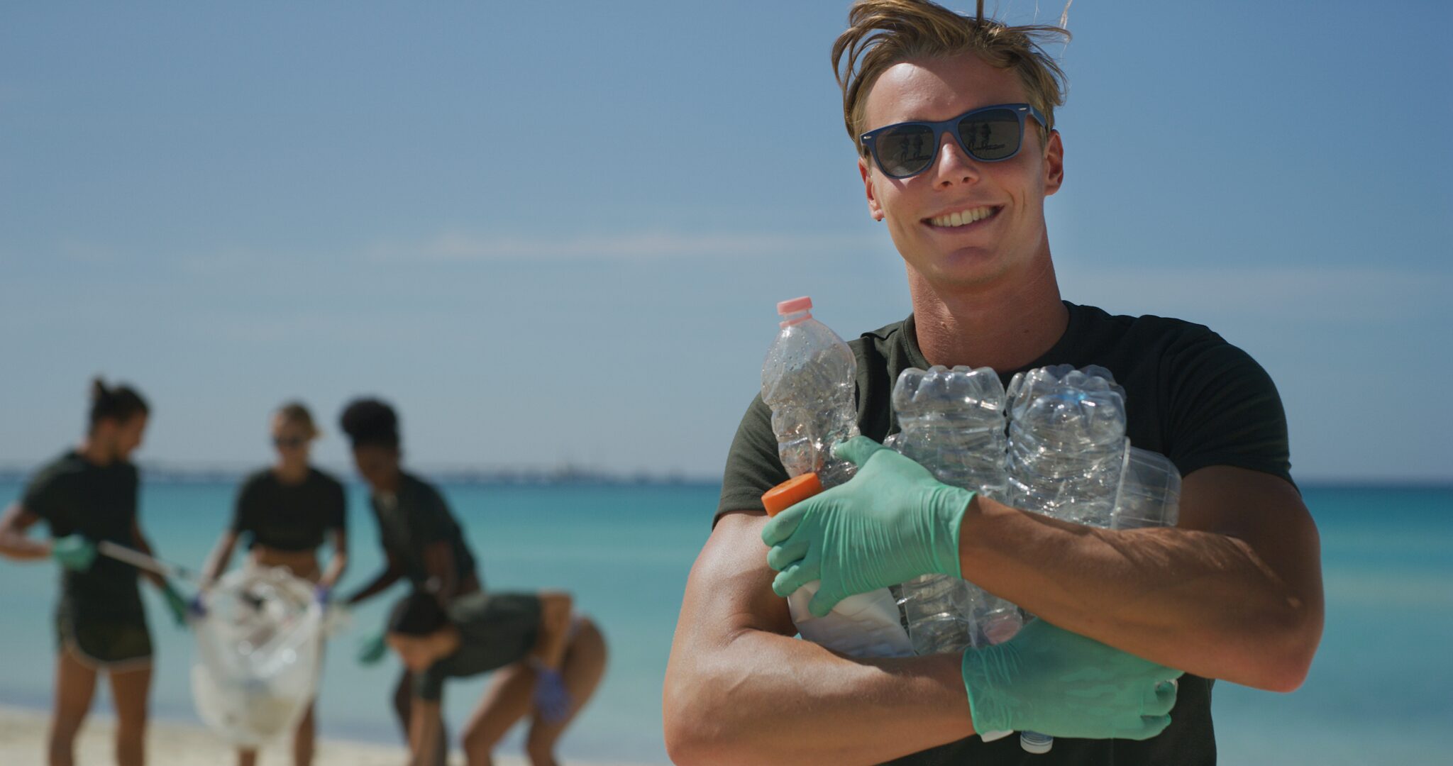 A young man in sunglasses cleans up plastic from a beach