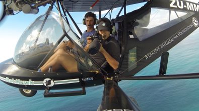 a marine scientist in a helicopter over the ocean holding a camera